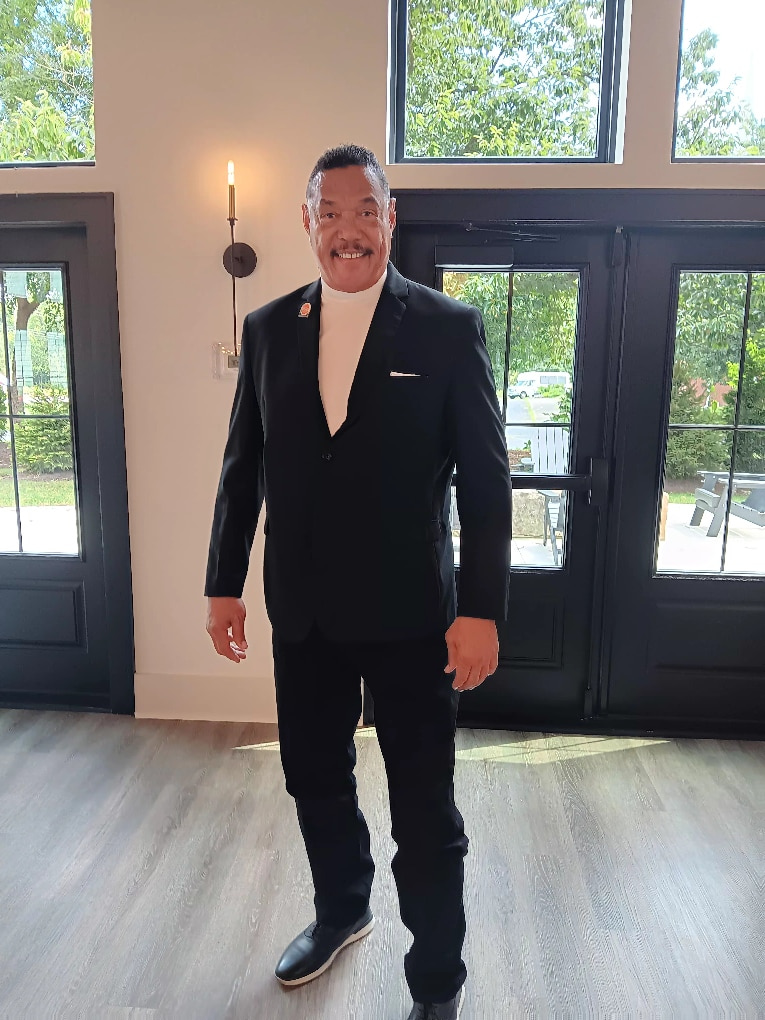 Coach Harvey Sims in a black suit jacket, smiling, photographed inside